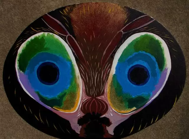 Painting of a stylized face or mask with large green and blue eye-like patterns, dark brown and black tones, artistic and mysterious